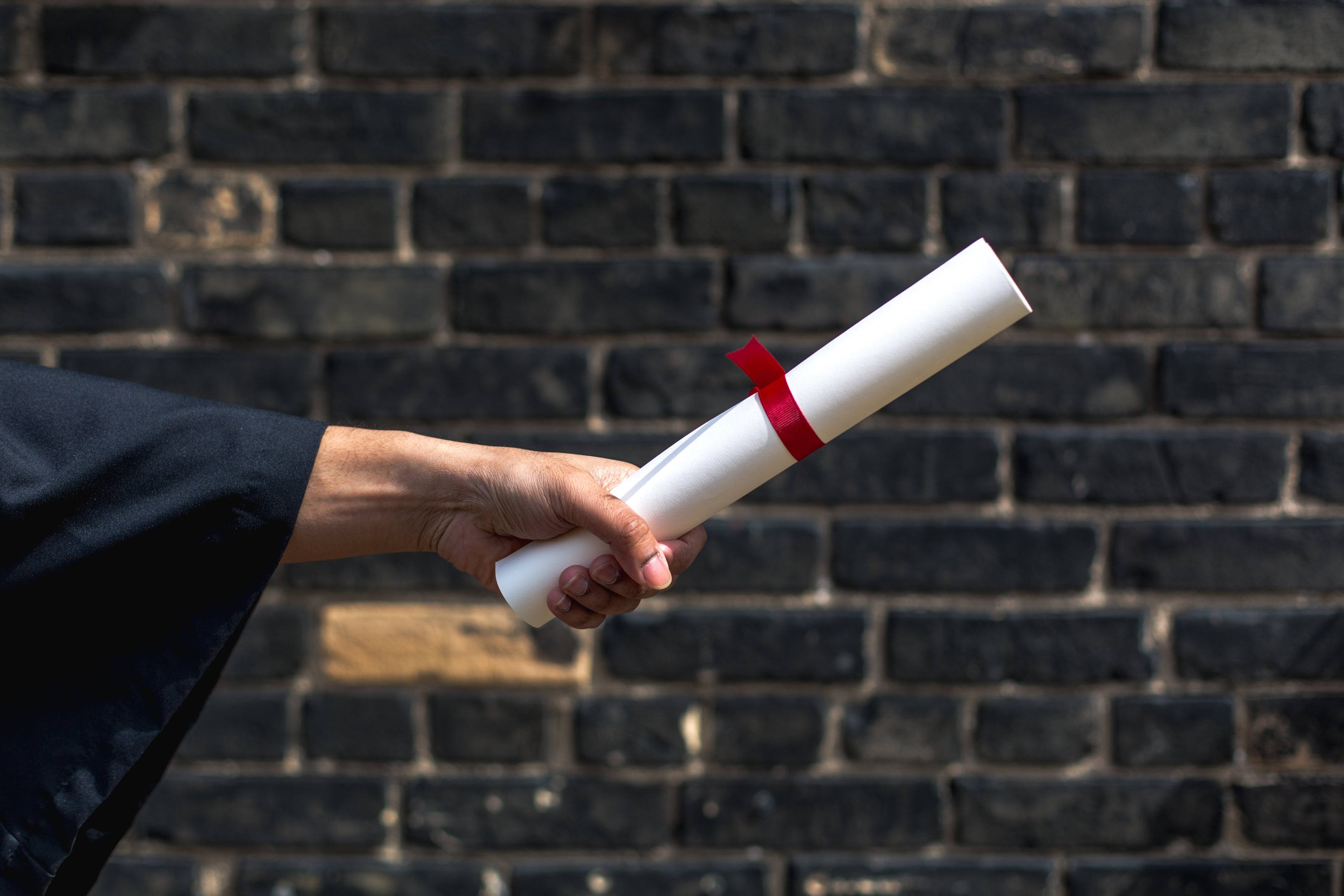 student-holding-out-diploma-by-wall